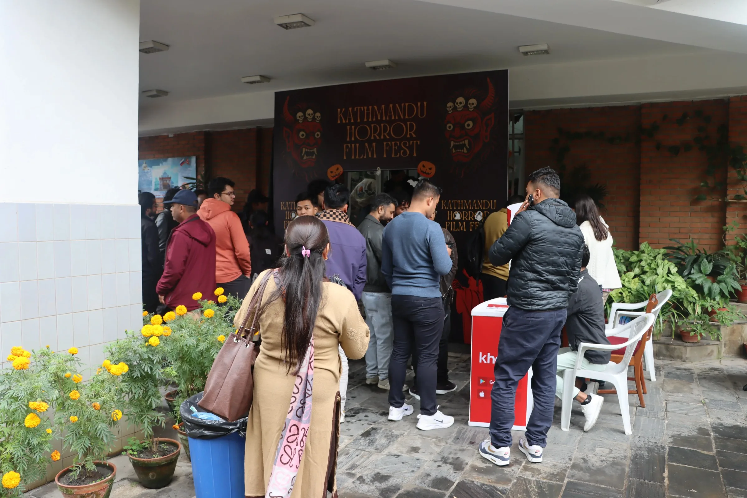 Audience queueing outside the venue at the Kathmandu Horror Film Fest, in front of a painted backdrop of red masked deities