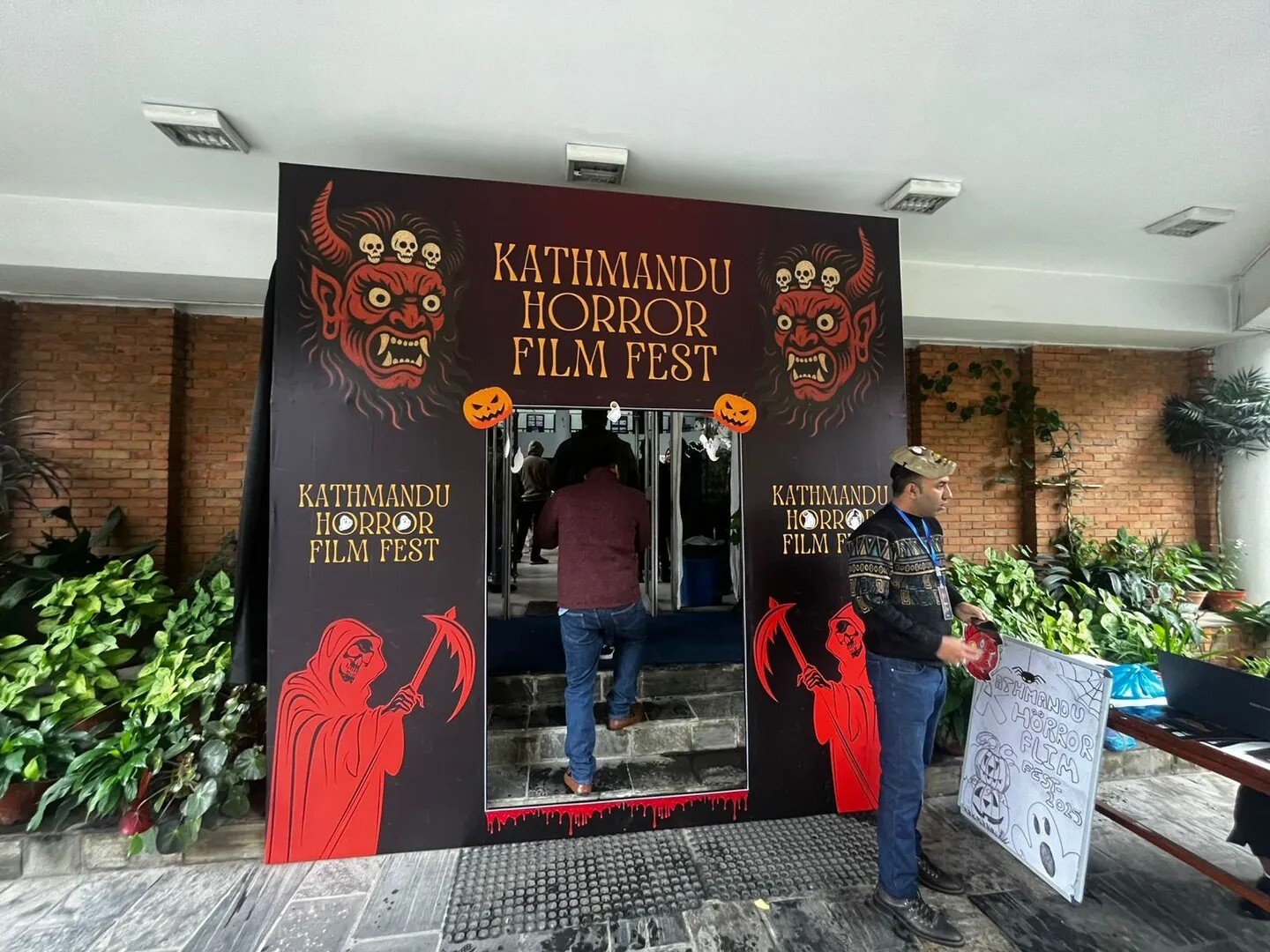 The Kathmandu Horror Film Fest entrance archway, painted with red masked deities and reapers, with an attendee walking through into the venue